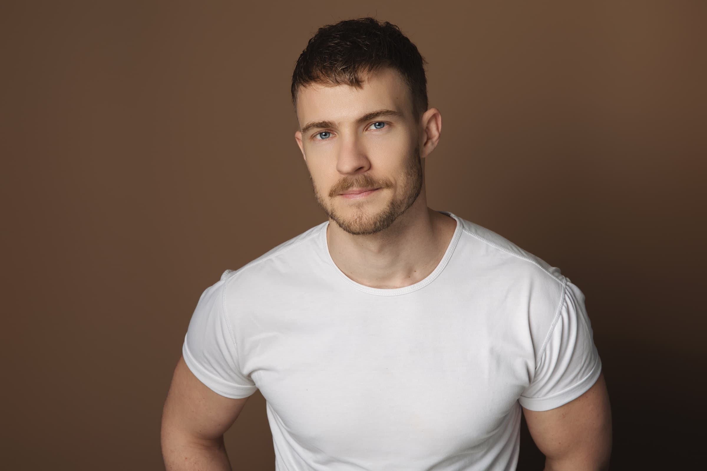 Close portrait of Aidan Wharton in a white t-shirt against a warm tan backdrop.