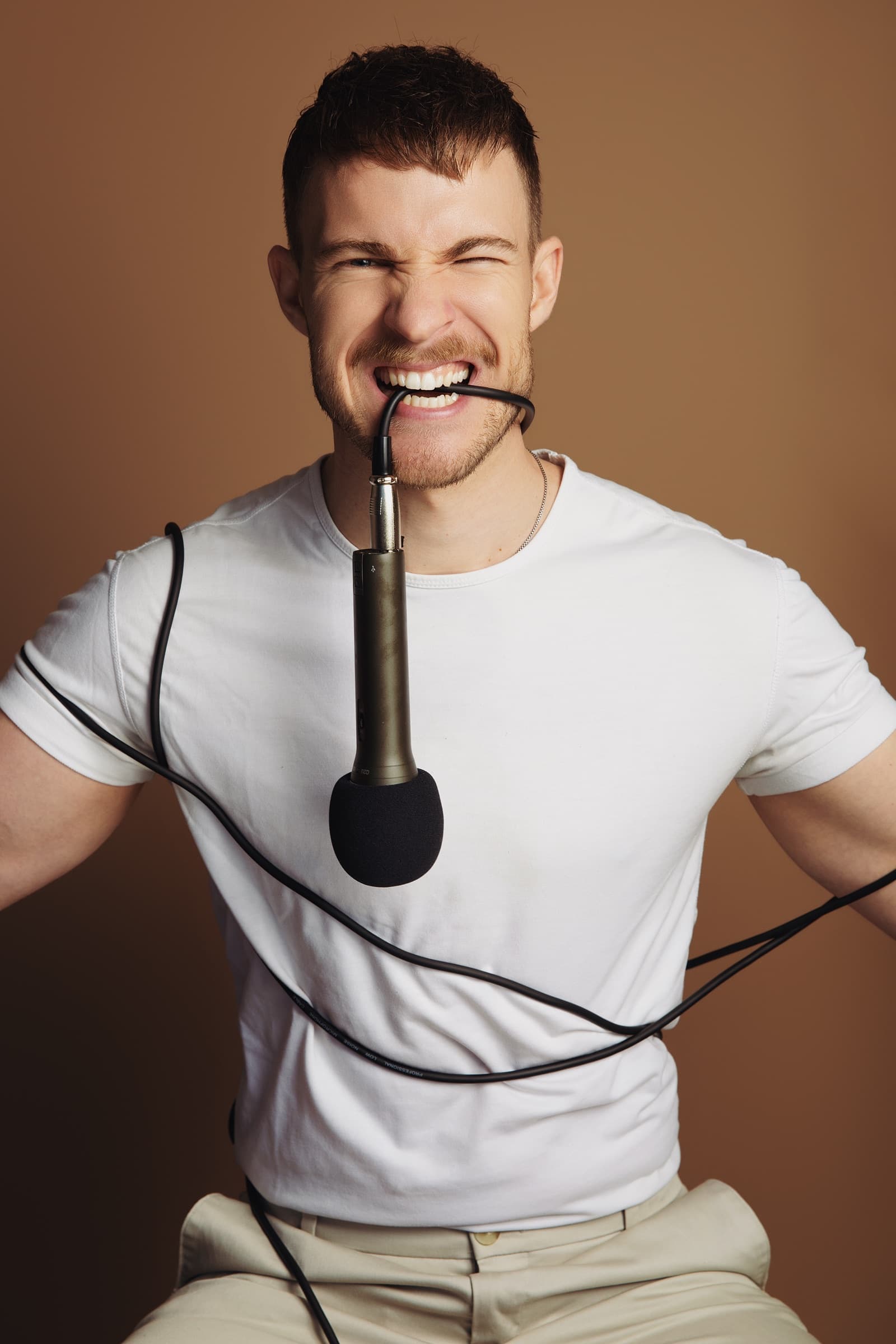 Aidan Wharton with a podcast microphone, laughing, the cable wrapped around his arms.
